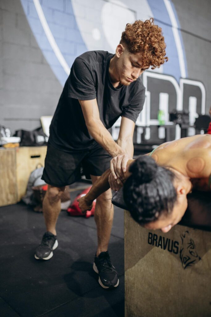 A therapist assisting with shoulder mobility and recovery in an indoor gym setting.