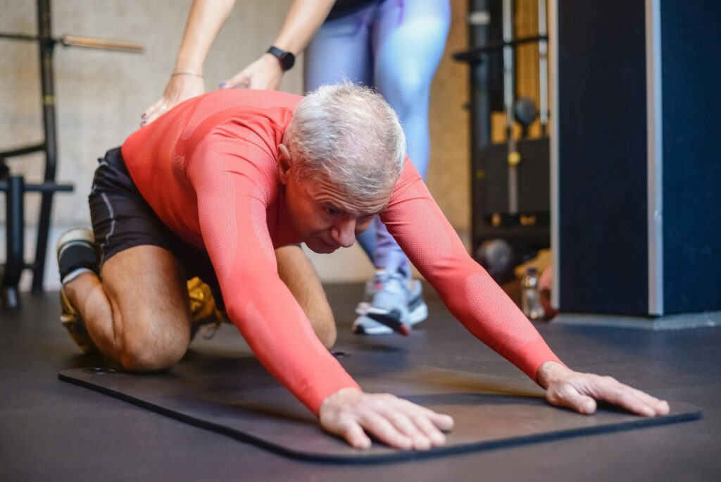 In-home personal trainer helping an elderly man with assisted stretching to improve mobility.